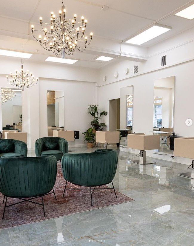 Hairdressing salon illuminated by large chandeliers and panel lights.